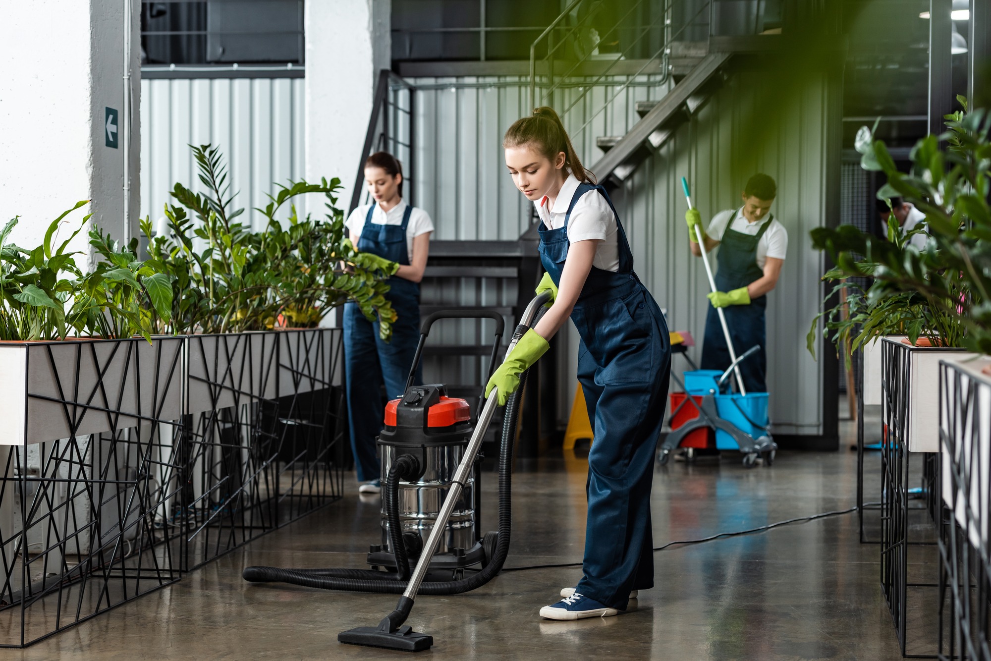 Young cleaner vacuuming floor in office
